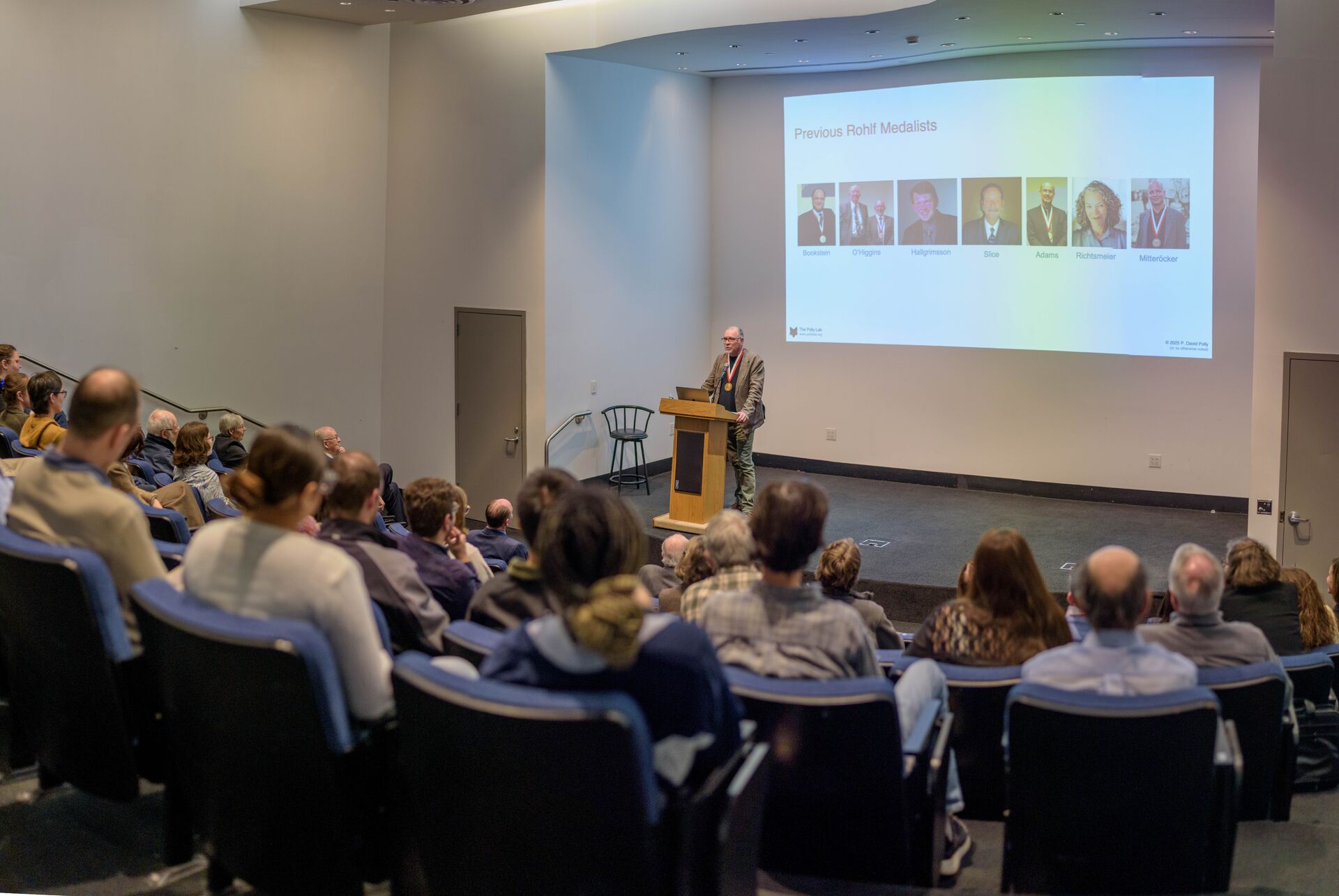 A wide view of P. David Polly delivering his Rohlf Medal lecture, showing a portion of the crowd in the lecture hall