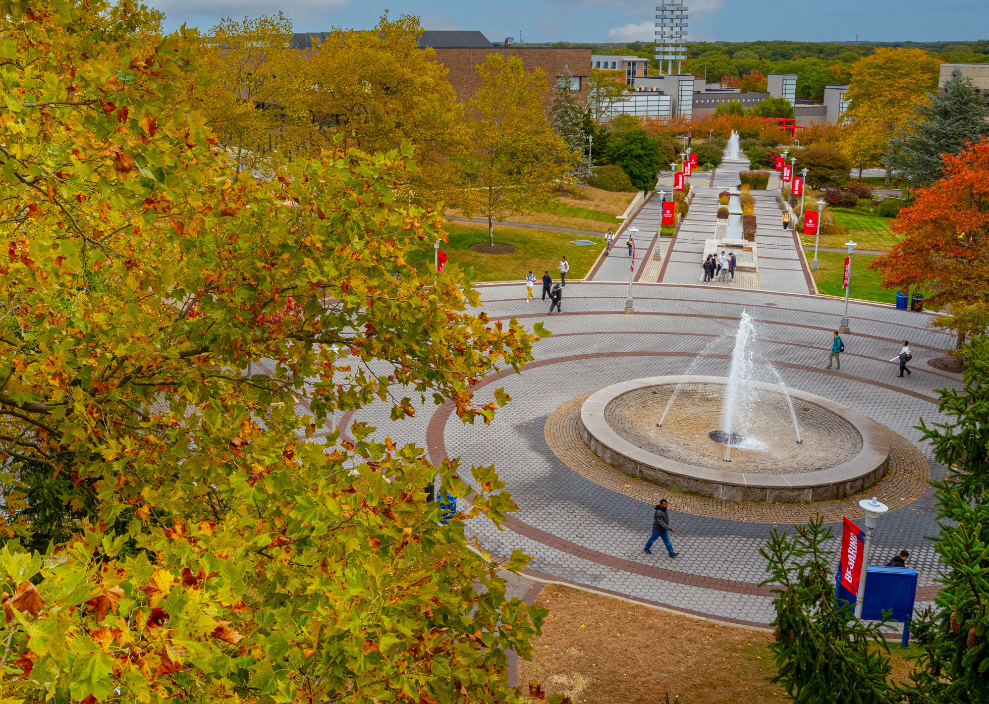 Aerial view of a Stony Brook University campus with a fountain and walkway, surrounded by trees and modern buildings