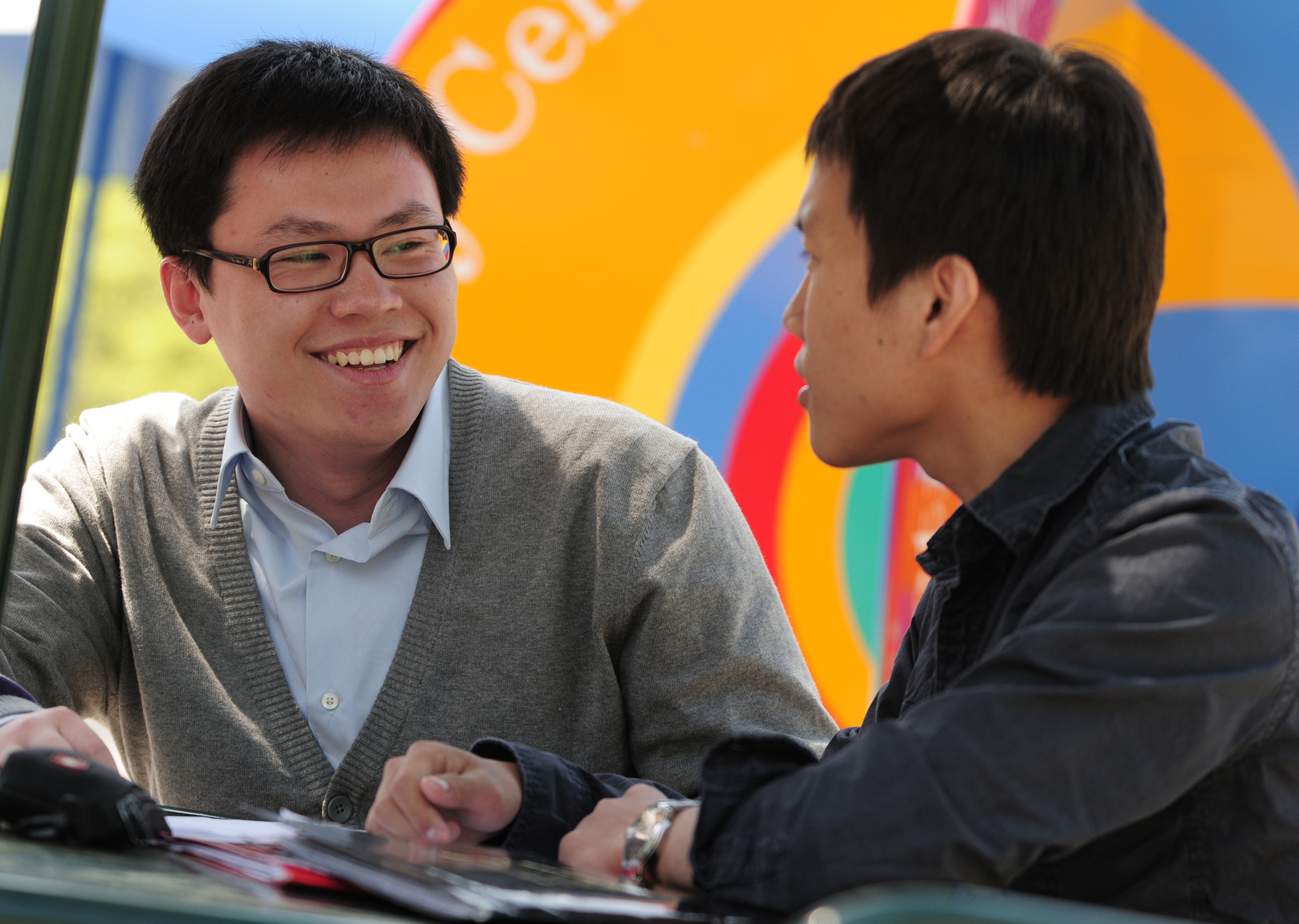 Two people seated at a table, smiling and talking, with a colorful background