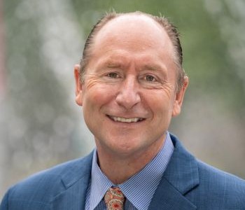 David Wrobel, wearing a blue suit, striped light blue shirt and patterned orange tie