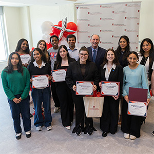 Group of diverse students holding certificates standing in front of balloon arch and backdrop