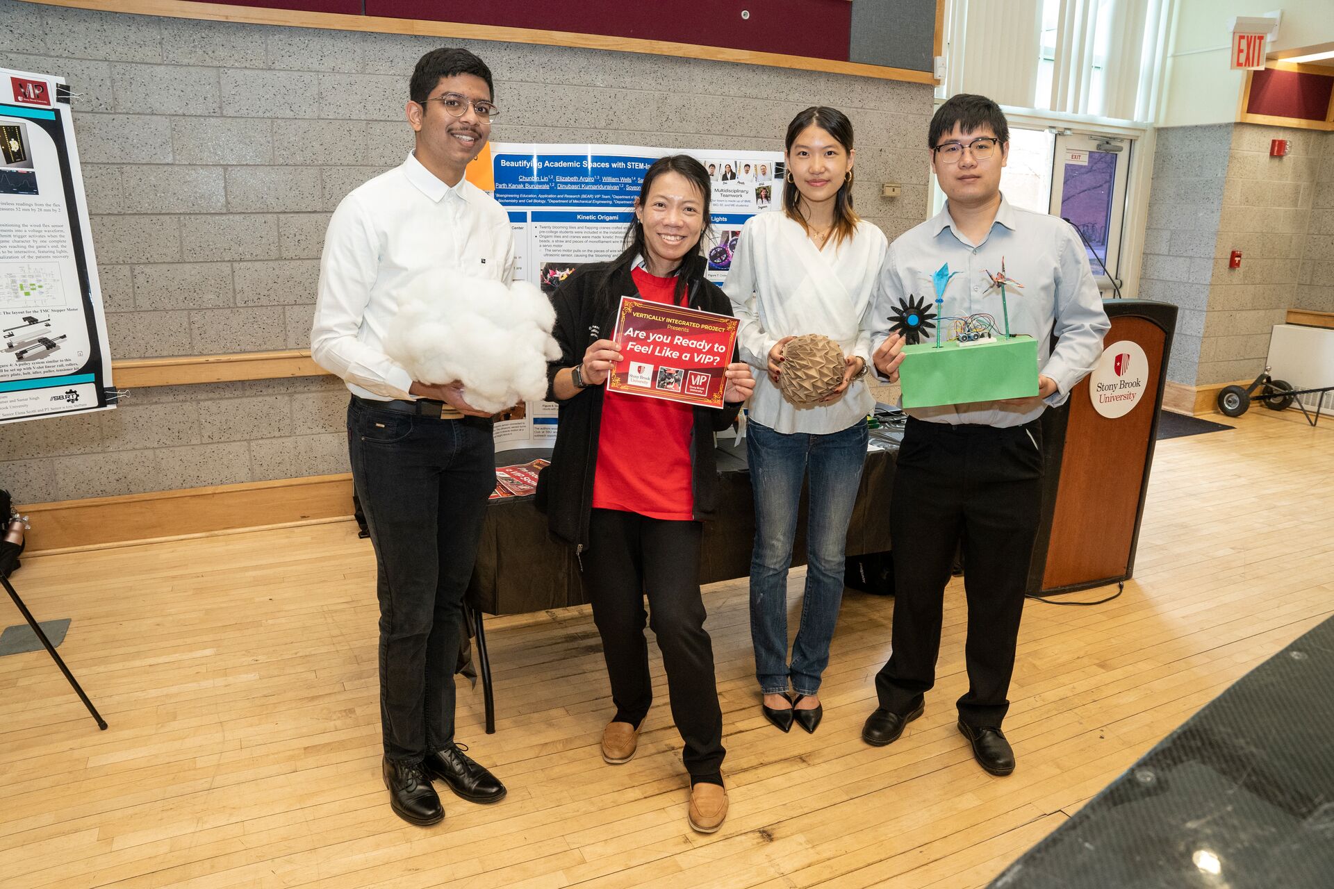 Four individuals posing in front of research posters and holding up flyers.