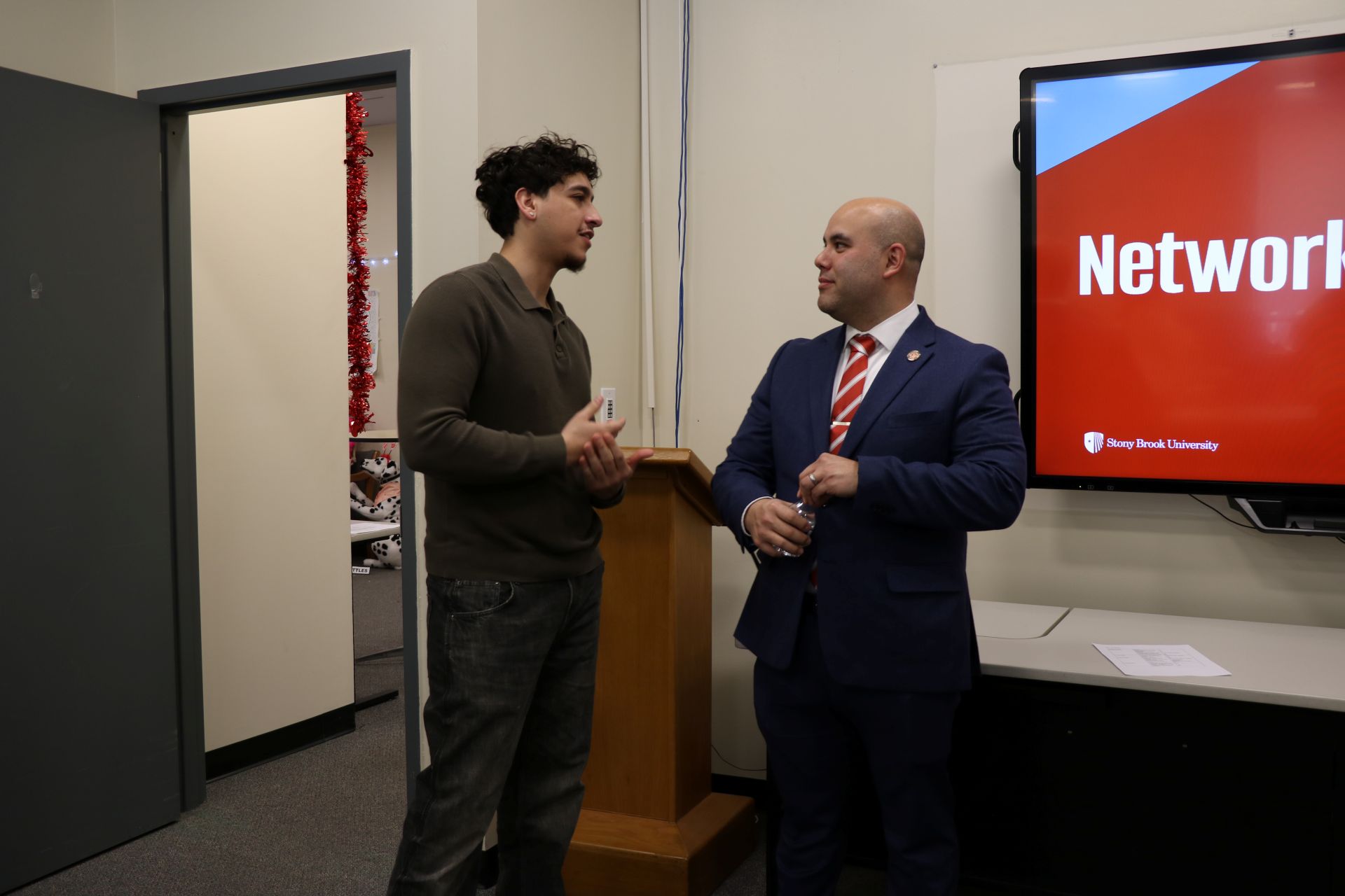 Two people standing in a classroom engaged in discussion.