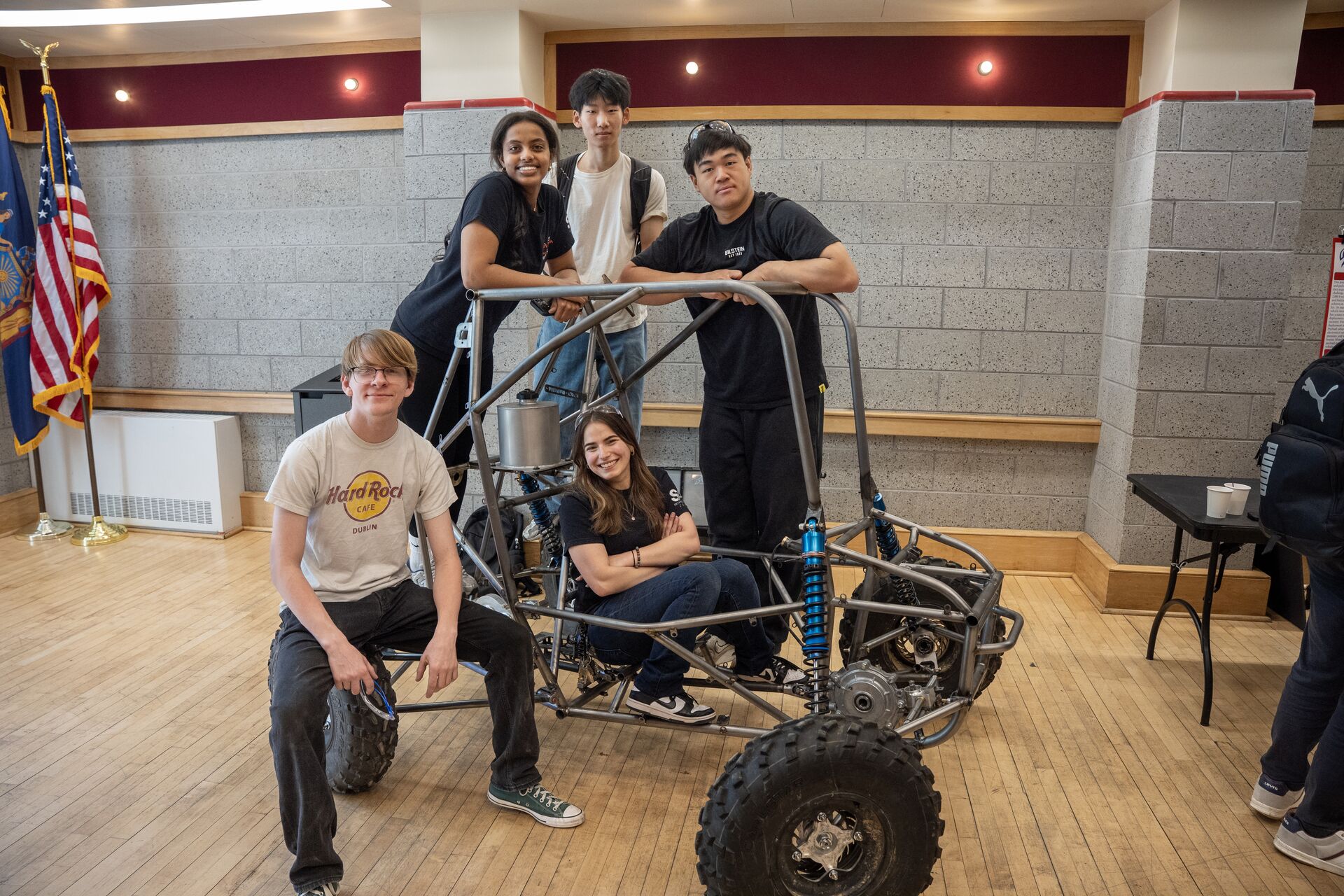 Students sitting and standing on the frame of a off-terrain vehicle.