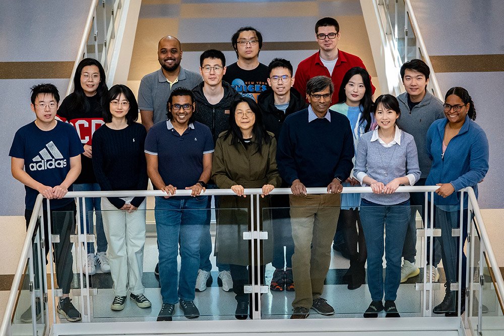 A group of sixteen people stand on a staircase, smiling at the camera.