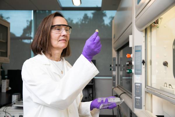 A scientist holding up her findings wearing white lab coat and purple gloves.
