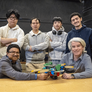 A group of six people stand and sit around a table displaying a colorful drone.