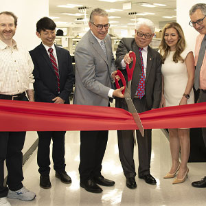 Six people cutting a red ribbon at a ribbon cutting event.