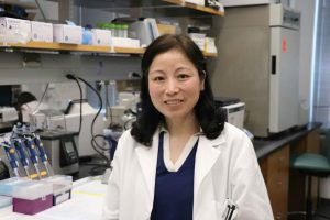 Wei Yin in a white lab coat standing in her lab.