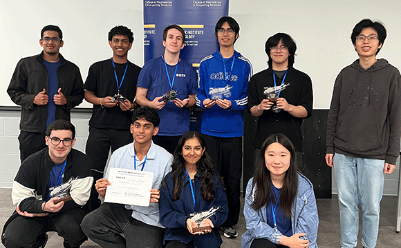 A group of smiling students holds trophies and a certificate, posing for a photo. They are dressed casually, conveying a sense of achievement and teamwork.