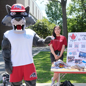 Wolfie, Stony Brook University mascot, standing with student in front of Origami Club table.