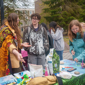 A group of students engages at an outdoor informational table, with colorful materials and pamphlets.