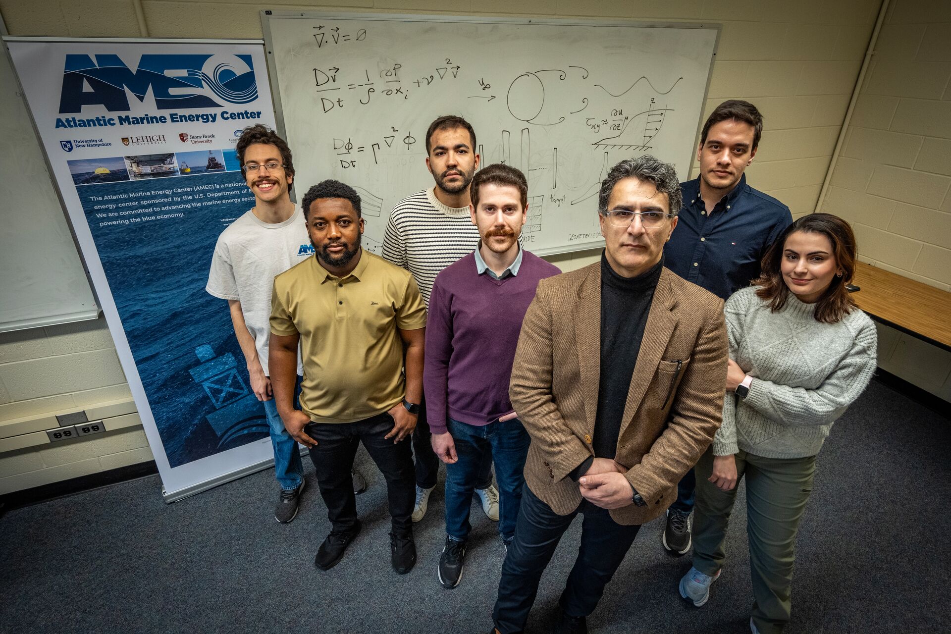 Researchers from the Atlantic Marine Energy Center posing in front of a whiteboard with fluid dynamics equations.