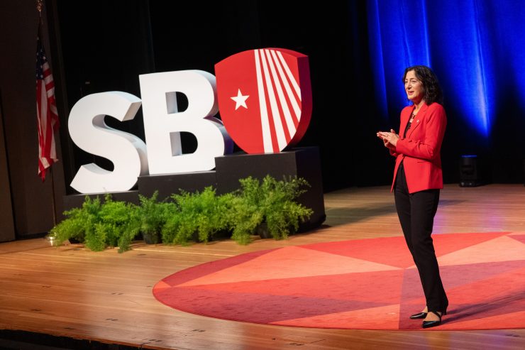President Andrea Goldsmith standing next to a large SBU sign, giving a State of the University address.