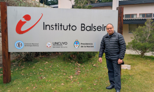 Professor Purwar poses next to the sign in front of Instituo Balseiro