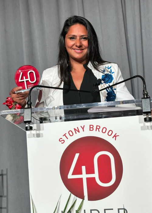 Shushanna Cherian-Brutus holds a 40 Under Forty Award while standing behind a lectern