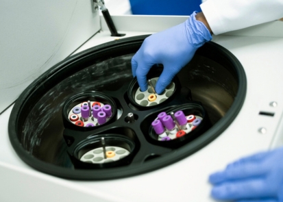 A gloved hand placing a vial of liquid into a centrifuge
