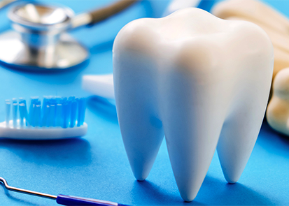 A large model tooth on a tray table beside a toothbrush and other dental tools
