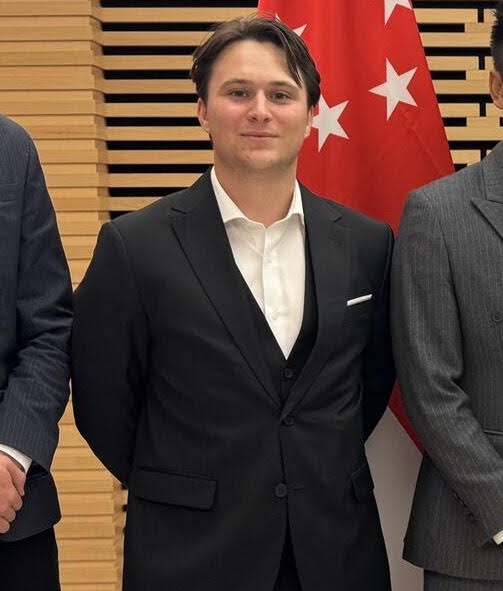 picture of student standing in front of a red flag wearing a suit