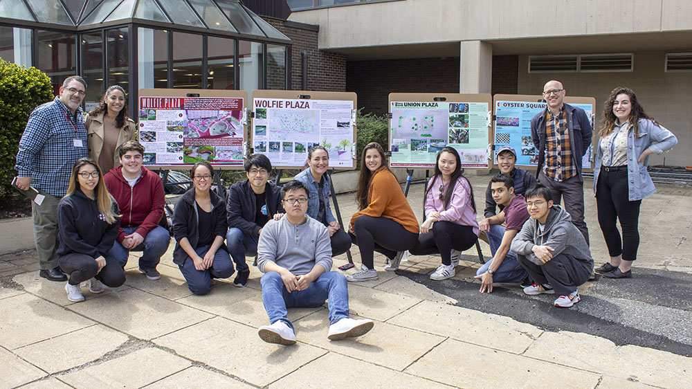 Dr. Donovan Finn and his EDP 404 class stand outside the Melville Library plaza with posters for proposed renovations