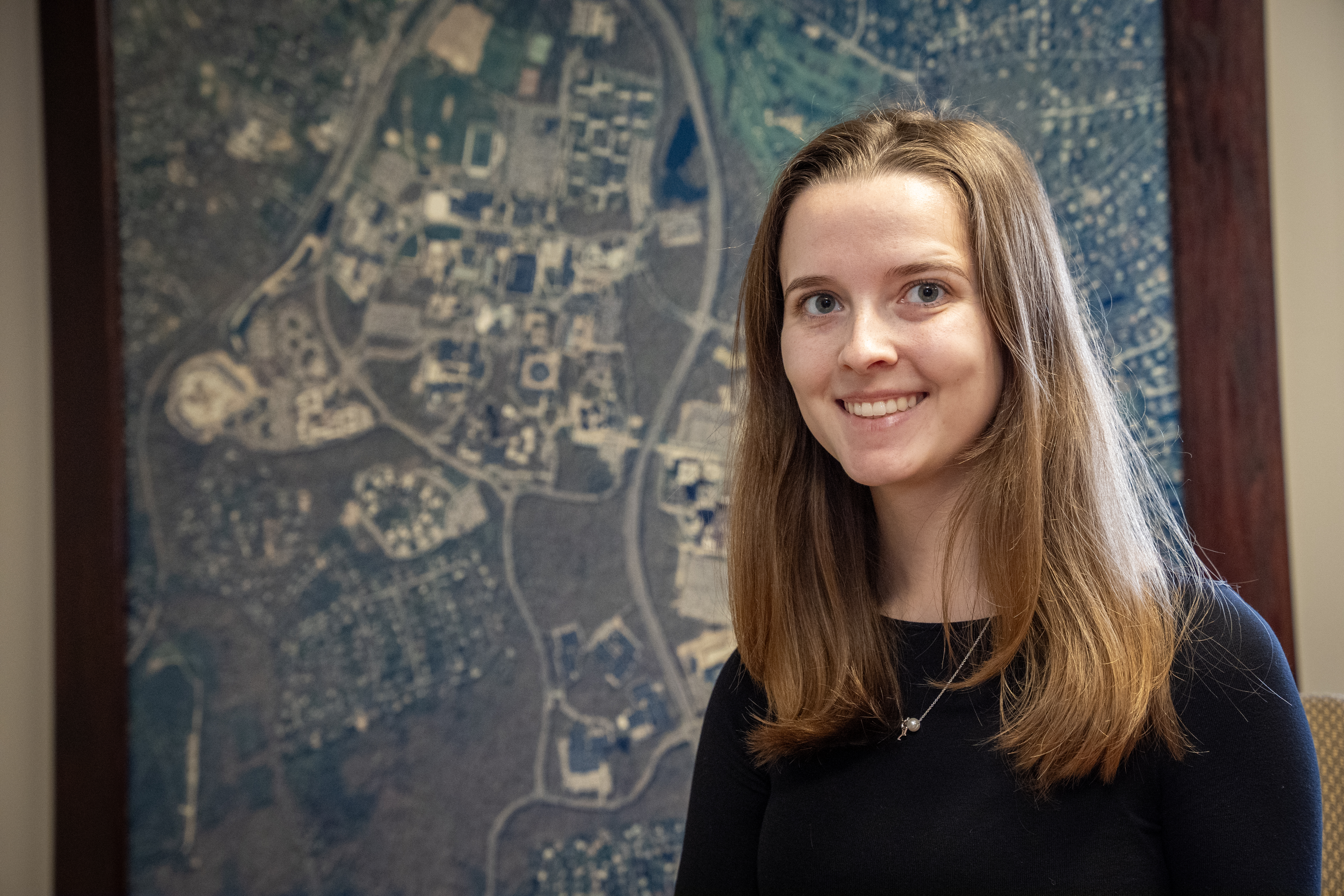 Caucasian woman with long blonde hair wearing black long sleeve shirt standing in front of aerial map