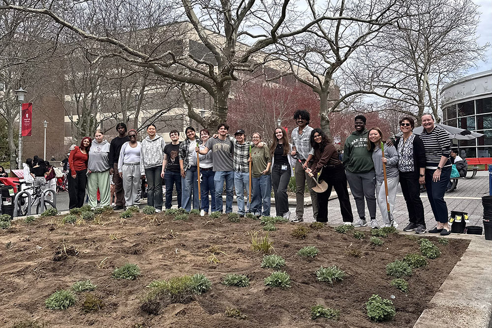 group of people standing behind a plant bed with shovels in their hand