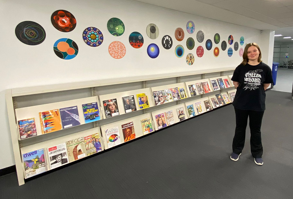 Student standing in front of record art display on the wall