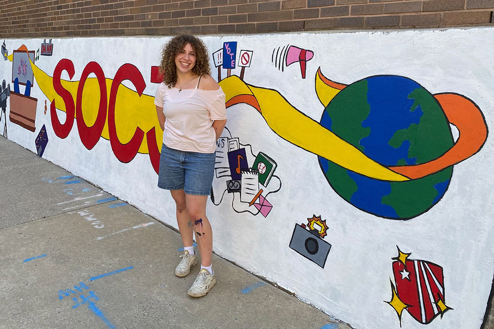 Student standing in front of painted SOCJ mural 