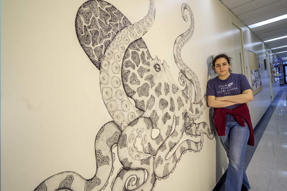 student stood next to the black and white octopus mural
