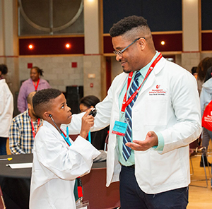 A medical student teaches a local elementary school student how to use a stethoscope. 