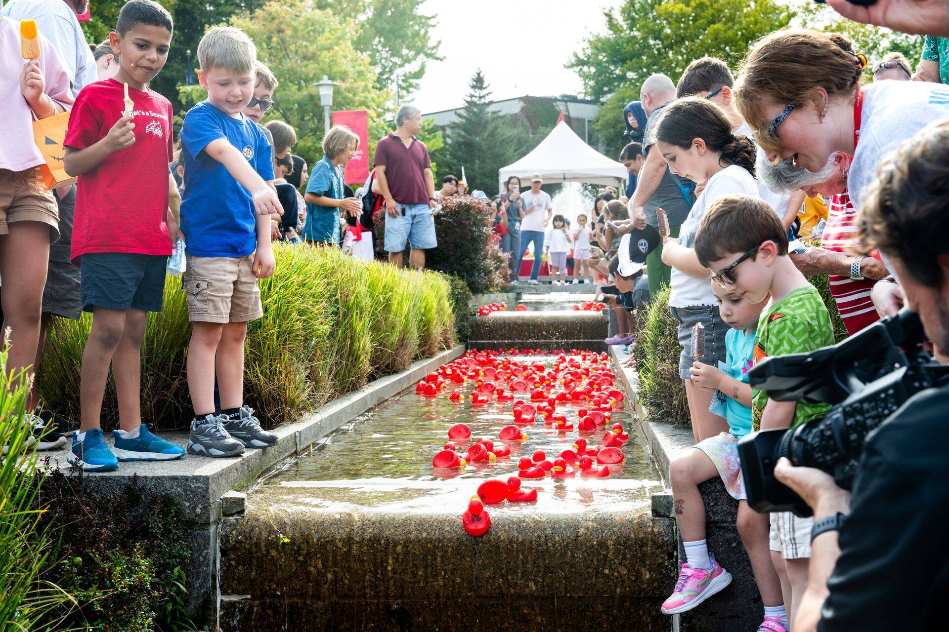 Kids observe red rubber ducks floating in a fountain.