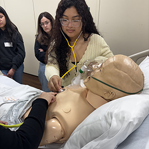 A student practices using a stethoscope in a lab setting.