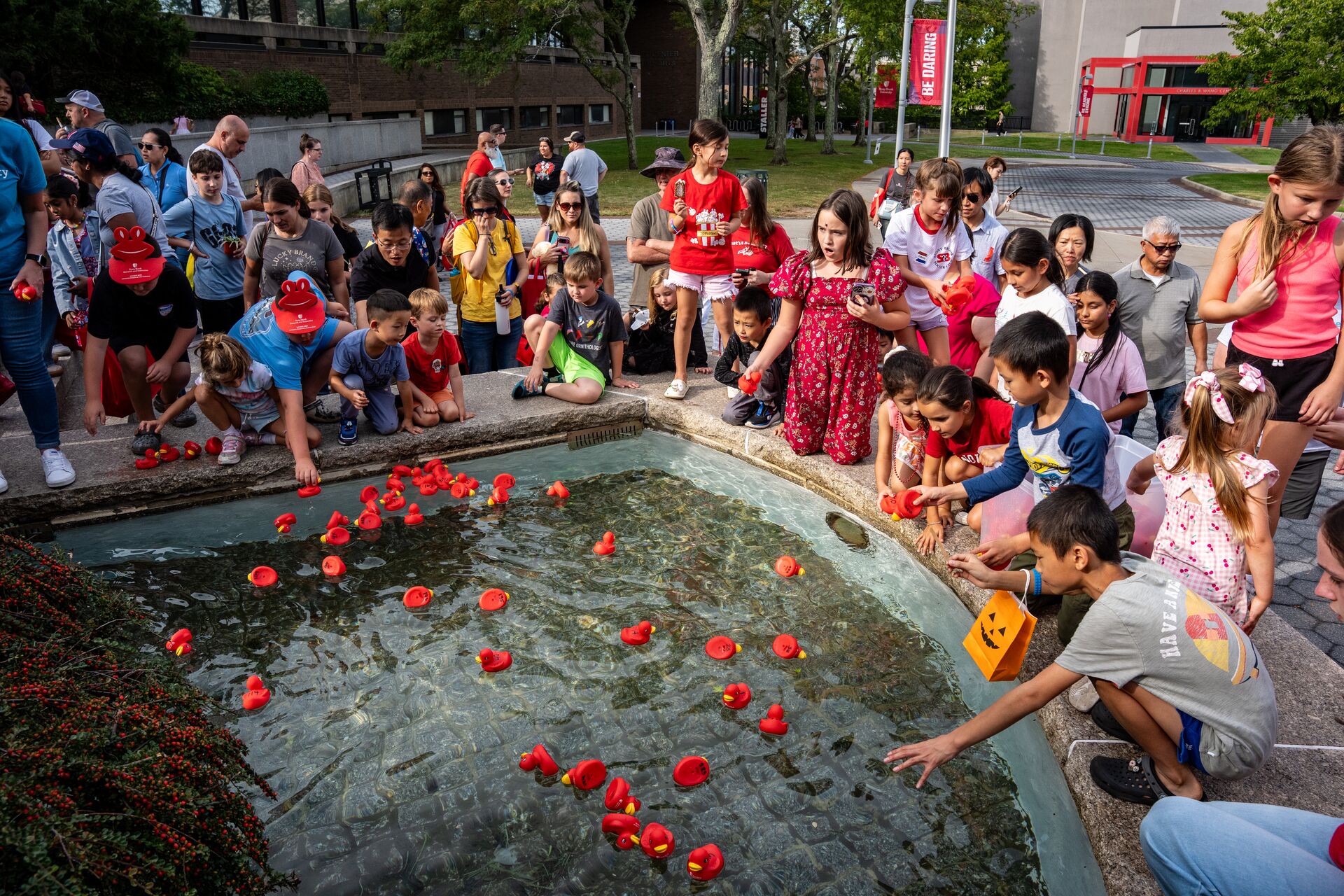 Attendees reach for red ducks floating in a fountain.