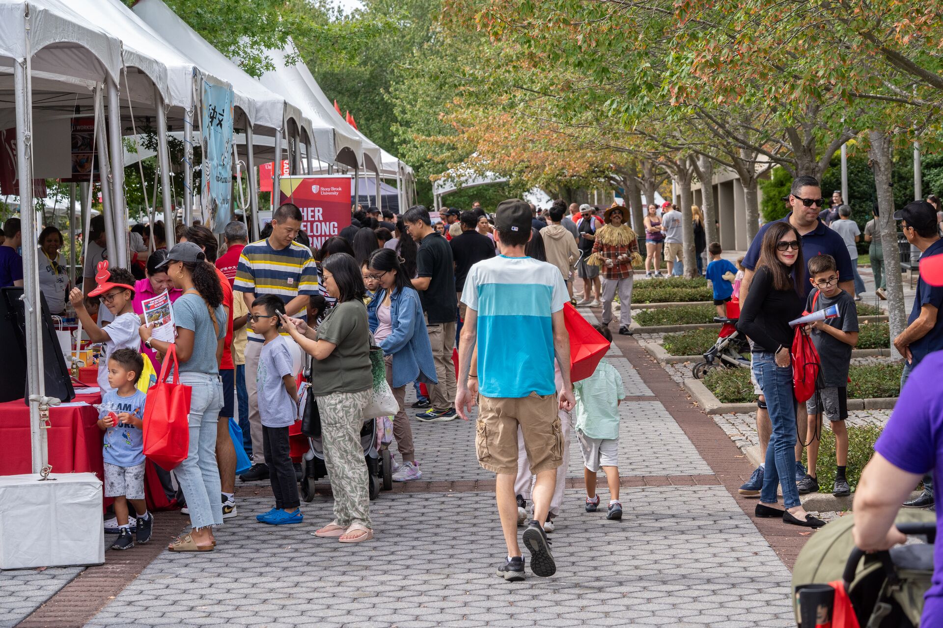 Attendees walk past a line of white tents at a festival.