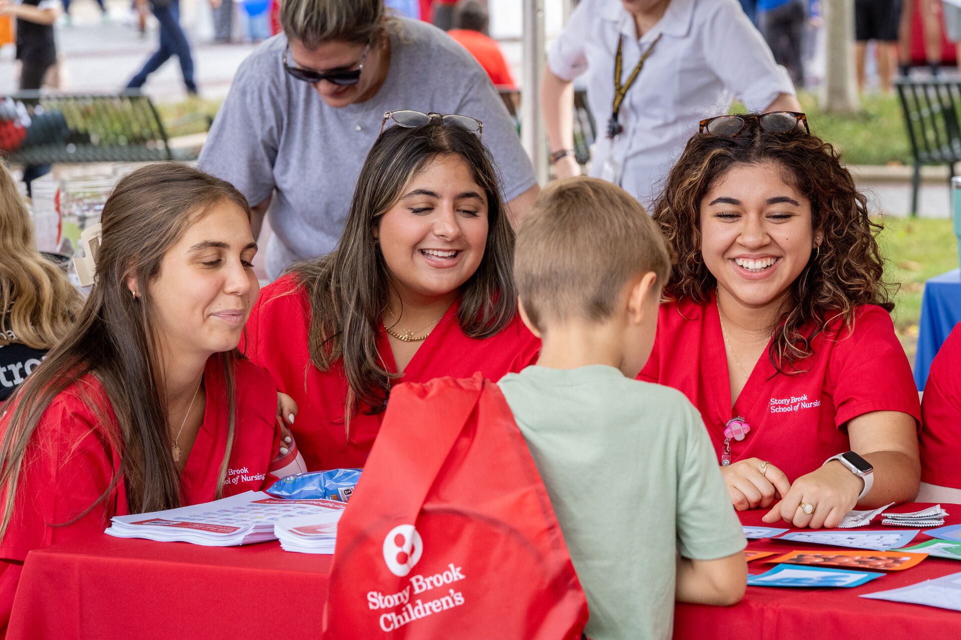 Three nursing students in red scrubs share educational materials.