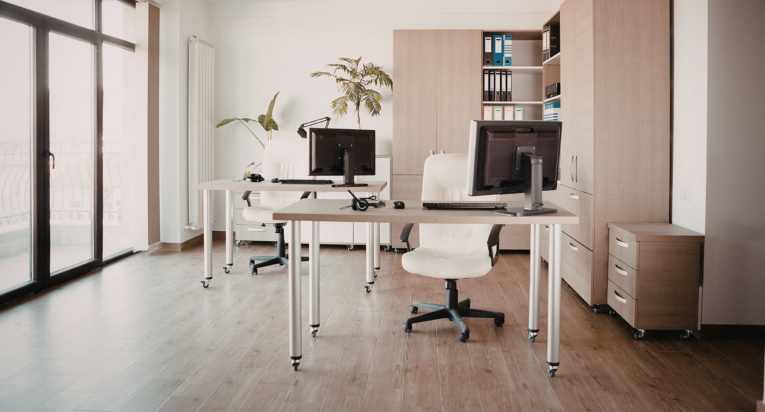 nuetral colored office space with two empty desks and cabinets on wall