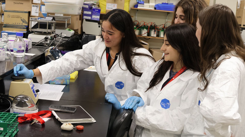 High school students wearing white lab coats performing experiments