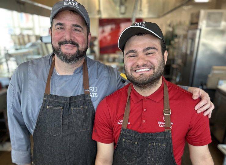 Two smiling people in aprons standing in a kitchen