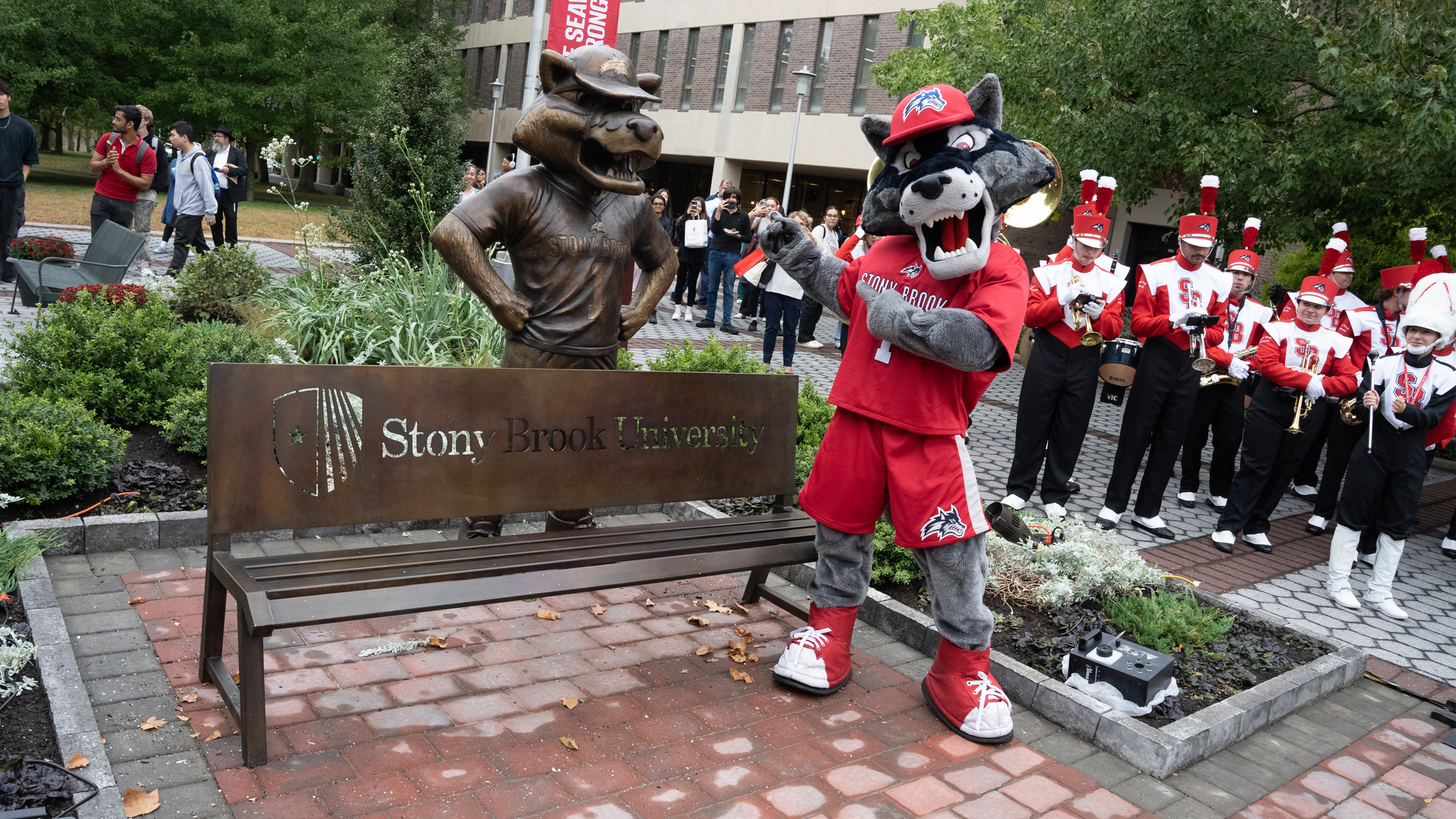 wolfie mascot standing near wolfie statue and bench