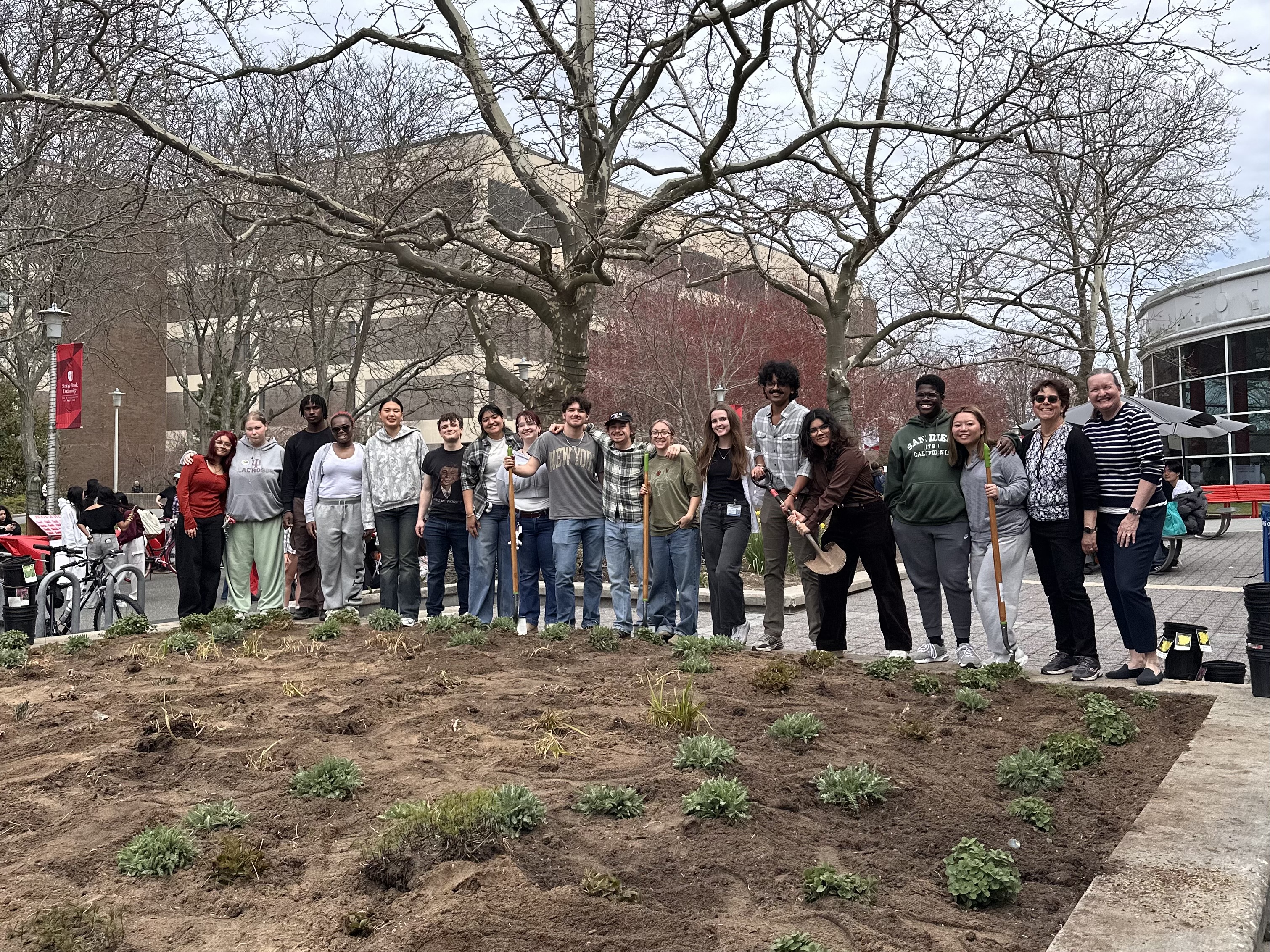Students and faculty pose with shovels in front of newly planted pollinator garden