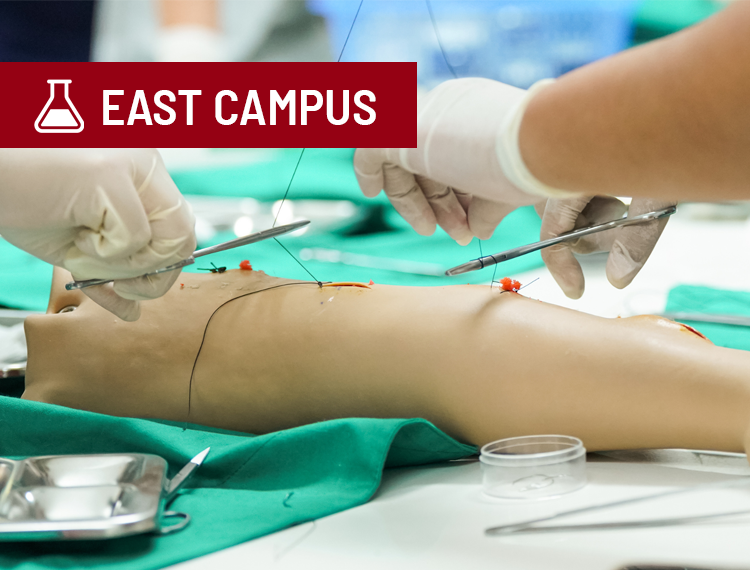 medical student hands suturing dummy arm with "East Campus" location label overlay