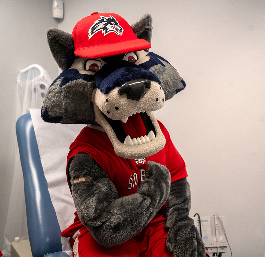 Wolfie in a doctor office chair flexing his arm to show off a bandaid.