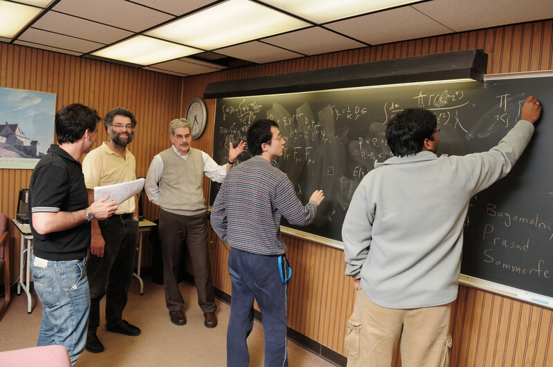 Students and faculty discussing equations at a chalkboard