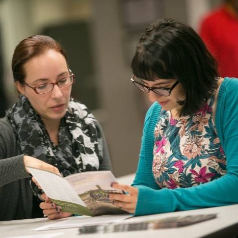 Two people sitting at a desk looking at a brochure
