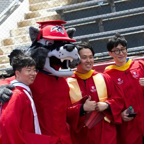 Three graduating students standing next to Wolfie