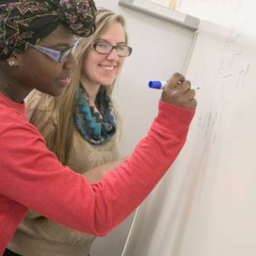 Two students writing on a white board