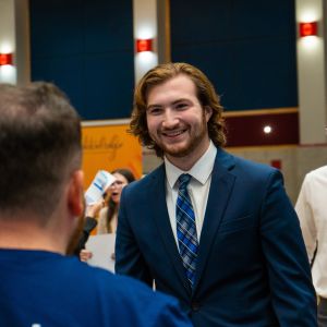 Student in professional attire speaking with others at a career event