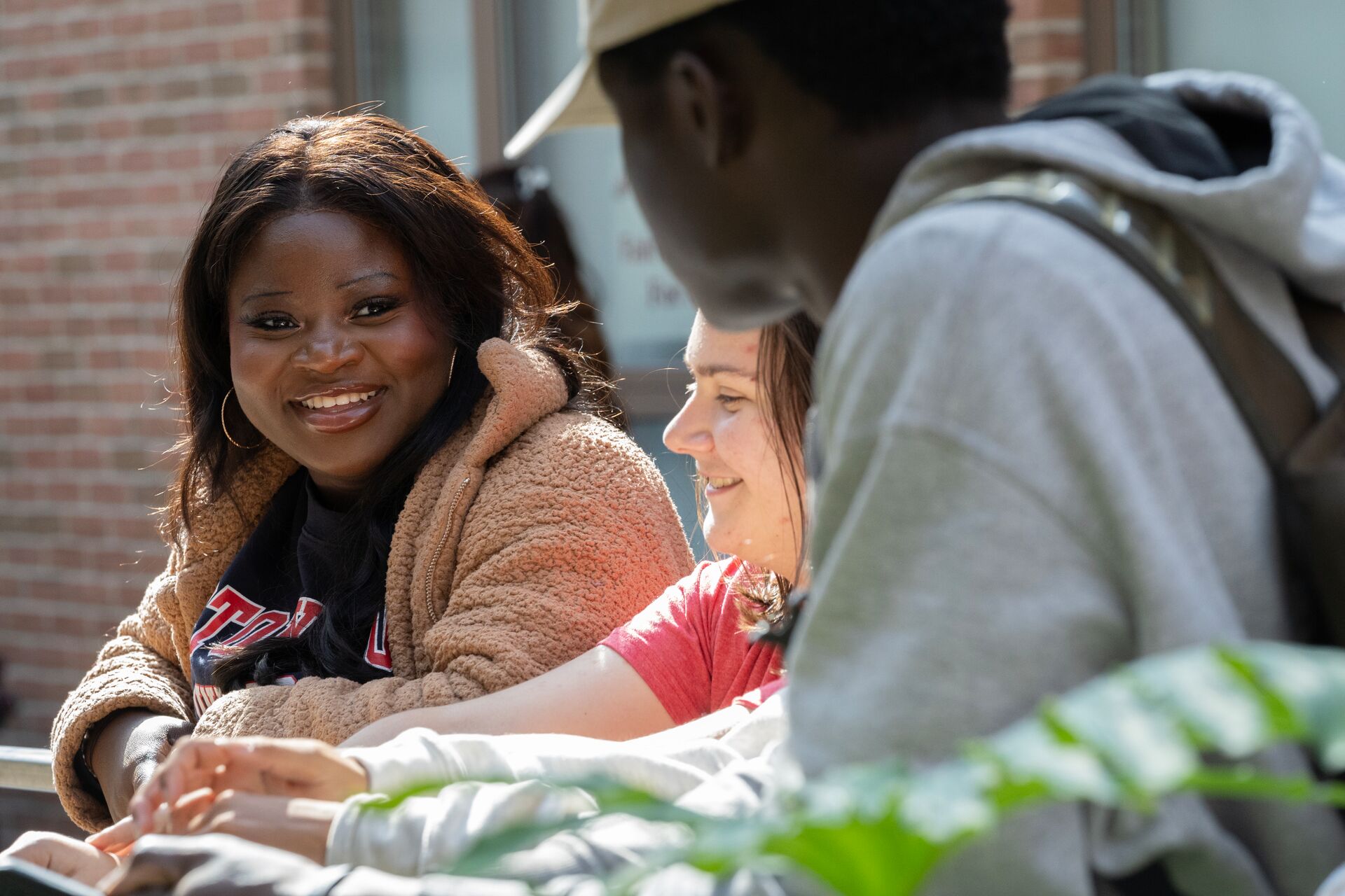 Three students talking outside while working on their computer
