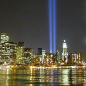 An image of NYC skyline with blue searchlights representing the two  fallen World Trade Center towers