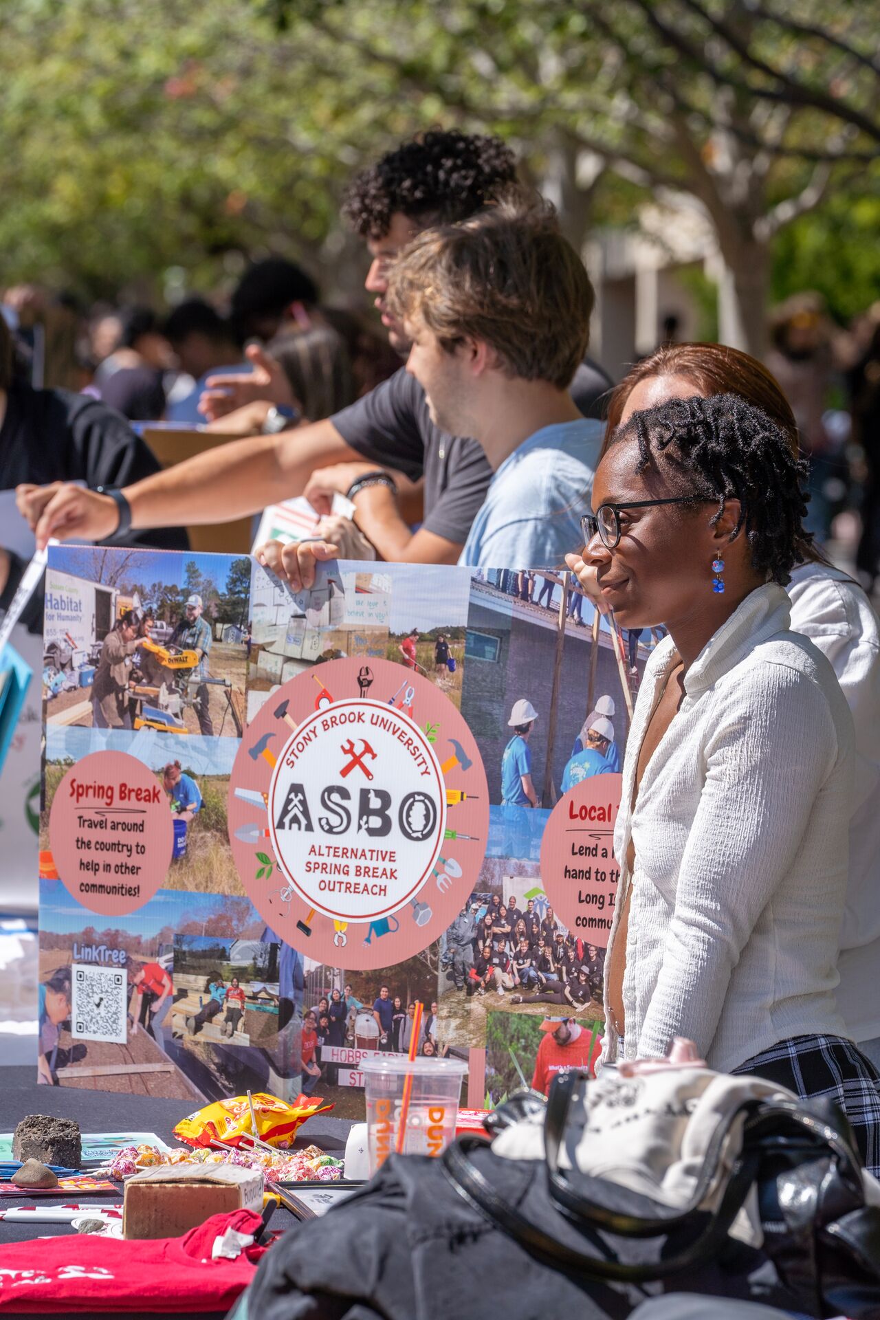 A student at a table promoting Stony Brook University's Alternative Spring Break Outreach, with colorful posters and various items displayed.